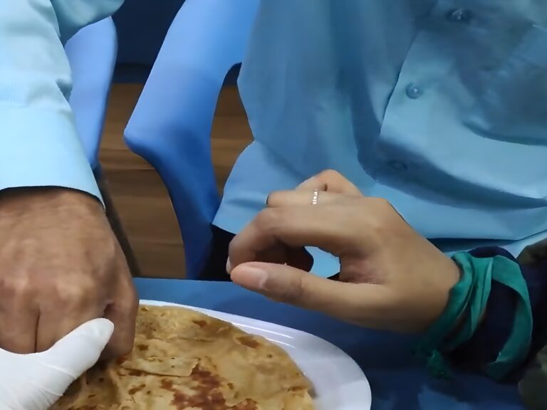 An adult's hand helping guide a child's hand toward a plate of roti, during a Kikstart occupational therapy feeding-support session